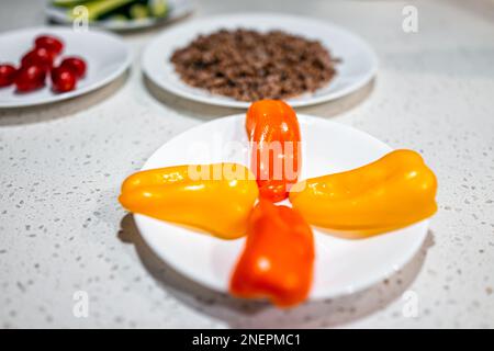In Scheiben geschnittene, farbenfrohe, süßgelbe, orangefarbene Paprika auf weißem Teller mit Tomaten und Buchweizenkörnern im Bokeh-Hintergrund Stockfoto