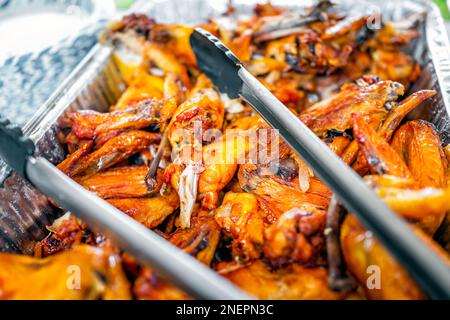 Brasilianisches barbecue mit Hähnchenbeinen und Flügeln mit Banketttablett und Metallzangen für gegrillte Fleischhaut und niemand Stockfoto