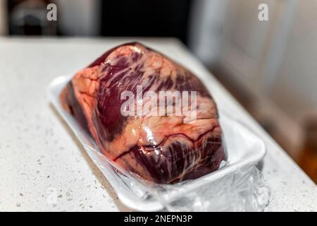 Rindfleisch-Ganzherz-Paket vom Metzger auf Plastiktablett mit Texturnaht von Muskelfleisch und niemand auf dem Küchentisch Stockfoto