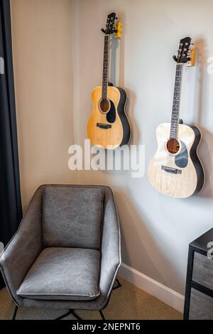 Wohnzimmereinrichtung mit Sessel und hängenden Akustikgitarren an der Wand für Musiker in modernem Haus Stockfoto