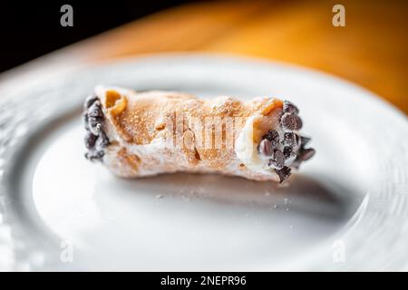 Italienisches Cannolo Gebäck Dessert auf weißem Plattenmakro mit Textur aus gelber Kruste und Buttercreme gefüllt mit Schokoladenstückchen in Cannoli Stockfoto