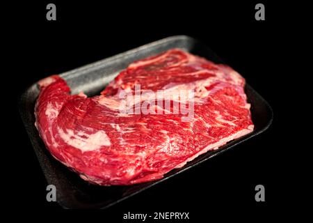 Verpacktes rohes Rindfleisch, schwarzes angus-Steak-Nahaufnahme mit schwarzem Hintergrund, Studioaufnahme mit fettmarmoriertem Tablett Stockfoto