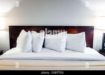 Schlafzimmer mit beleuchtetem Lampenlicht und Blick auf weiße Kissen mit Laken auf leerer Matratzenauflage im modernen Hotel mit Niemand Stockfoto