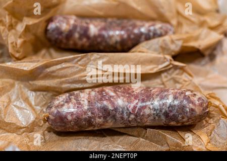 Zwei italienische Schweinewürste mit Plastikpapiermetzgerpackung, mit Hülse und Fett auf Fleisch Stockfoto