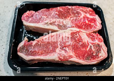 Zwei rote rohe Streifensteaks Fleischstückchen Makro der Konsistenz vom Metzger, geschnitten auf Plastiktablett in der Küche Stockfoto
