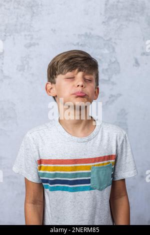 Ein süßer kleiner Junge mit Autismus in einem Studio, der ein schmieriges Gesicht mit geschlossenen Augen macht Stockfoto