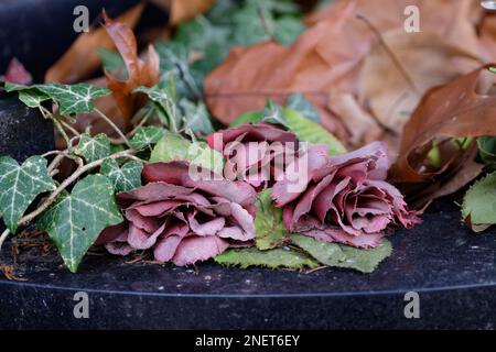 Alte verblasste künstliche Rosen auf einem verlassenen Grab eines Friedhofs Stockfoto