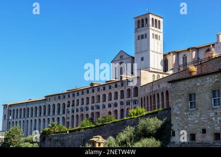 Seitenansicht der Basilika des Heiligen Franz von Assisi und des Heiligen Konvents mit seinem Glockenturm unter einem klaren blauen Himmel Stockfoto
