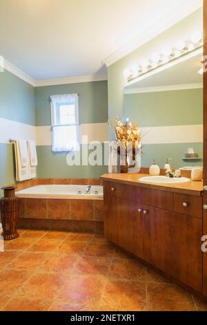 Rostfarbener Melaminholztisch mit geschichteter Arbeitsfläche und eingeschlossener Badewanne im oberen Badezimmer mit Keramikfußfliesen und großem Spiegel. Stockfoto