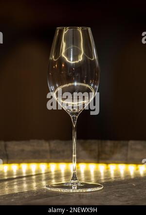 Eine vertikale Aufnahme eines leeren Weinglases auf dem gelb beleuchteten Tisch Stockfoto