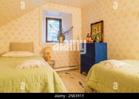 Zwei Einzelbetten mit hellgrünen Bettüberwürfen und antiker blauer Kommode aus Holz im Gästezimmer mit weiß bemalten Pinienholzböden im alten Haus. Stockfoto