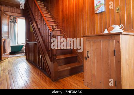 Waschstand und Holztreppe führen zum Dachboden und öffnete Tür zum Hauptbadezimmer mit grüner und weißer Krallenfußbadewanne im alten 1927-Jahre-Haus. Stockfoto