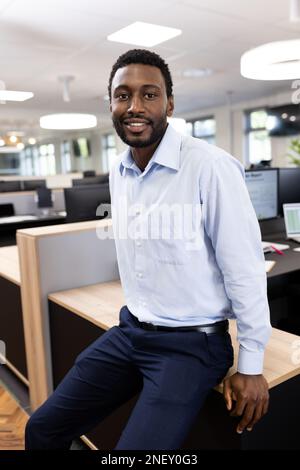 Vertikales Bild eines glücklichen afroamerikanischen Geschäftsmanns, der im Büro vor die Kamera schaut Stockfoto