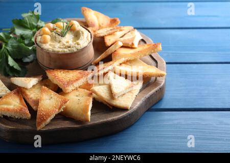 Köstliche Pita-Chips mit Hummus auf blauem Holztisch, Nahaufnahme Stockfoto