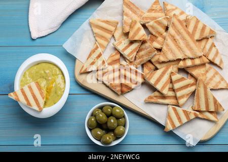 Leckere Pita Chips, Oliven und Hummus auf hellblauem Holztisch, flach liegend Stockfoto