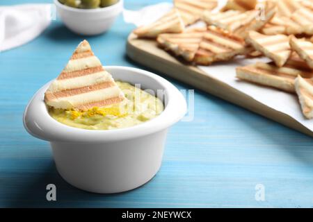 Köstliche Pita Chips und Hummus auf hellblauem Holztisch, Nahaufnahme Stockfoto