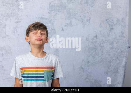 Ein süßer kleiner Junge mit Autismus in einem Studio, der ein schmieriges Gesicht mit geschlossenen Augen macht Stockfoto