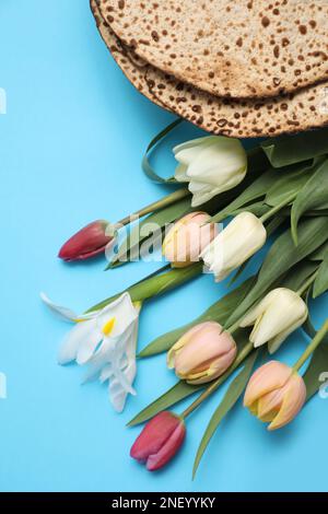 Leckere Matzen und frische Tulpen auf hellblauem Hintergrund, flach liegend. Pessach-Feier Stockfoto