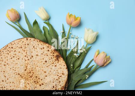 Leckere Matzen und frische Blumen auf hellblauem Hintergrund, flach liegend. Pessach-Feier Stockfoto