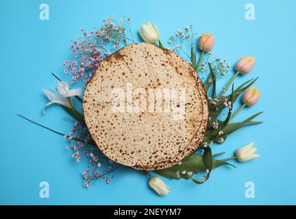 Leckere Matzen und frische Blumen auf hellblauem Hintergrund, flach liegend. Pessach-Feier Stockfoto