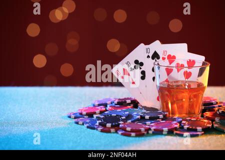 Alkoholgetränk, Spielkarten und Casino-Chips auf dem Tisch gegen verschwommenes Licht. Eine vierfache Pokerkombination Stockfoto