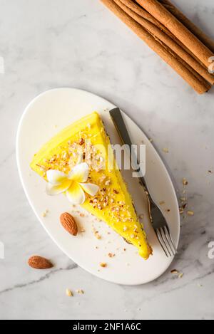 Ein Stück Karottenkuchen mit Sahne, mit Mandelkrümeln bestreut, auf einem weißen Teller auf einem Marmorhintergrund Stockfoto