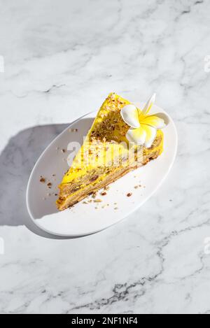 Ein Stück Karottenkuchen mit Sahne, mit Mandelkrümeln bestreut, auf einem weißen Teller auf einem Marmorhintergrund Stockfoto