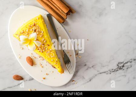 Ein Stück Karottenkuchen mit Sahne, mit Mandelkrümeln bestreut, auf einem weißen Teller auf einem Marmorhintergrund Stockfoto