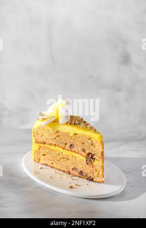 Ein Stück Karottenkuchen mit Sahne, mit Mandelkrümeln bestreut, auf einem weißen Teller auf einem Marmorhintergrund Stockfoto