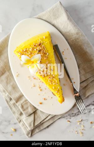 Ein Stück Karottenkuchen mit Sahne, mit Mandelkrümeln bestreut, auf einem weißen Teller auf einem Marmorhintergrund Stockfoto