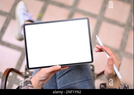 Draufsicht einer asiatischen Frau oder Freiberuflerin, die ein digitales Tablet zum Entspannen im Freien verwendet. Tablet-Modell mit weißem Bildschirm Stockfoto