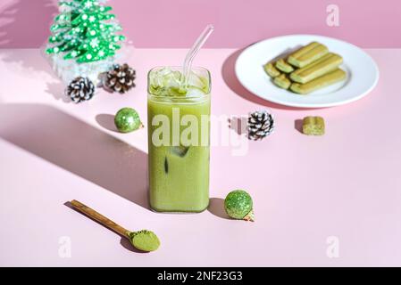 matcha Latte des neuen Jahres. Ein Glas Eistee steht auf pinkfarbenem Hintergrund neben Weihnachtsbällen und einem Weihnachtsbaum Stockfoto