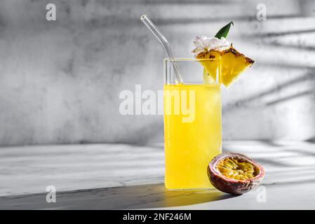 Ananas mit Passionsfruchtsaft. Auf grauem Hintergrund, Sonnenlicht, in Scheiben geschnittene Passionsfrüchte und Ananasstücke in der Nähe. Dekoriert mit einer Blume, Food St. Stockfoto