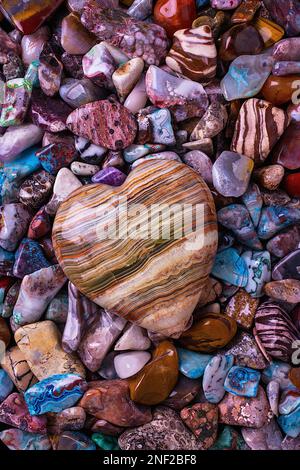 Herzförmiger Stein auf einem Haufen wunderschöner farbiger Steine und Felsen Stockfoto