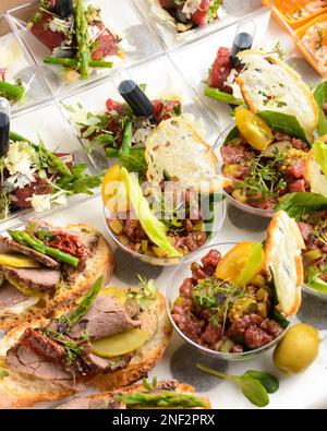 Verschiedene Snacks für das Catering im Licht. Tartare, Bruschetta, Salate, Kartoffeln, Törtchen zur Lieferung in einer Pappschachtel Stockfoto