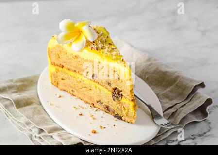 Ein Stück Karottenkuchen mit Sahne, mit Mandelkrümeln bestreut, auf einem weißen Teller auf einem Marmorhintergrund Stockfoto