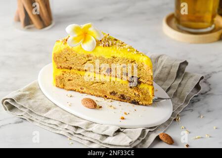 Ein Stück Karottenkuchen mit Sahne, mit Mandelkrümeln bestreut, auf einem weißen Teller auf einem Marmorhintergrund Stockfoto