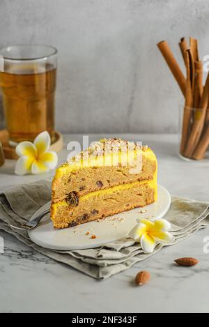 Ein Stück Karottenkuchen mit Tee. Der Kuchen liegt auf einem weißen Teller, verziert mit Mandeln, hinter einem Glas mit Zimtstangen und einem Glas Tee Stockfoto
