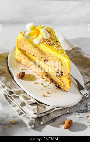 Ein Stück Karottenkuchen mit Sahne, mit Mandelkrümeln bestreut, auf einem weißen Teller auf einem Marmorhintergrund Stockfoto