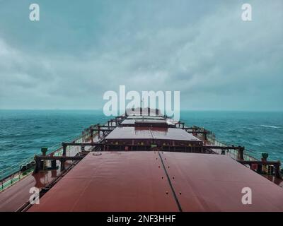 Eine lange Sicht auf ein großes Frachtschiff, das mitten auf dem Meer unter nebeligem, bedeckten Himmel segelt Stockfoto