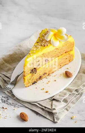 Ein Stück Karottenkuchen mit Sahne, mit Mandelkrümeln bestreut, auf einem weißen Teller auf einem Marmorhintergrund Stockfoto
