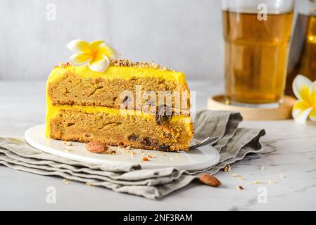 Ein Stück Karottenkuchen mit Tee. Der Kuchen liegt auf einem weißen Teller, verziert mit Mandeln, hinter einem Glas mit Zimtstangen und einem Glas Tee Stockfoto