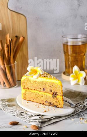 Ein Stück Karottenkuchen mit Tee. Der Kuchen liegt auf einem weißen Teller, verziert mit Mandeln, hinter einem Glas mit Zimtstangen und einem Glas Tee Stockfoto