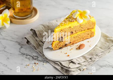 Ein Stück Karottenkuchen mit Tee. Der Kuchen liegt auf einem weißen Teller, verziert mit Mandeln, hinter einem Glas mit Zimtstangen und einem Glas Tee Stockfoto