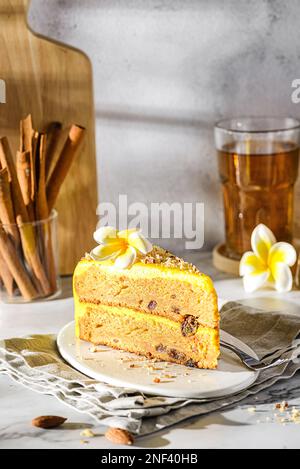 Ein Stück Karottenkuchen mit Tee. Der Kuchen liegt auf einem weißen Teller, verziert mit Mandeln, hinter einem Glas mit Zimtstangen und einem Glas Tee Stockfoto
