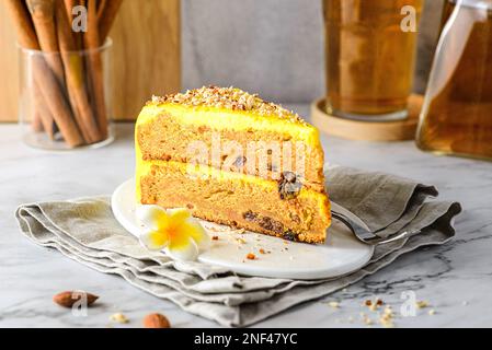 Ein Stück Karottenkuchen mit Tee. Der Kuchen liegt auf einem weißen Teller, verziert mit Mandeln, hinter einem Glas mit Zimtstangen und einem Glas Tee Stockfoto