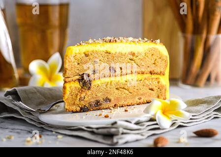 Ein Stück Karottenkuchen mit Tee. Der Kuchen liegt auf einem weißen Teller, verziert mit Mandeln, hinter einem Glas mit Zimtstangen und einem Glas Tee Stockfoto