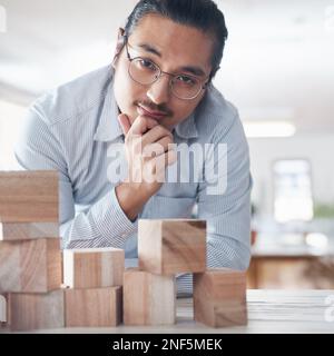 Jeder Block ist Teil der Lösung. Ein junger Geschäftsmann, der mit Holzbausteinen in einem modernen Büro arbeitet. Stockfoto
