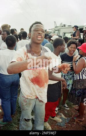 A Katlehong resident with blood over his clothes snarls at the press to leave on Sunday Jan. 9, 1994 in South Africa after an African National Congress convoy carrying ANC General Secretary Cyril Ramaphosa and South African communist Party leader Joe Slova, came under fire. A photographer for the Associated Press, Abdul Shariff was killed in the attack and two other journalists were wounded. (AP Photo/David Brauchli)