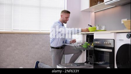 Junger Mann, Der Trinkglas Aus Der Spülmaschine In Der Küche Nimmt Stockfoto